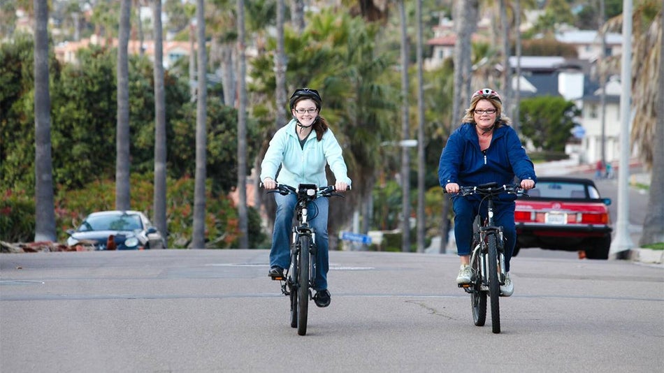 2 Women Riding Bikes Down a palm tree lined Street along La Jolla in San Diego, California, USA
