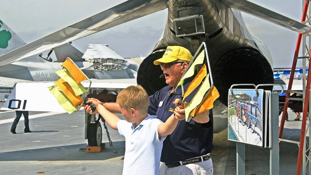 Child Waiving Flags with a tour guide in front of a plain at the USS Midway Museum - San Diego, California, USA