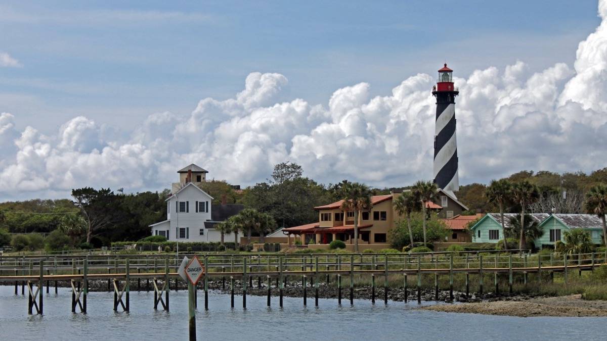 Wide shot of pier and ocean with St. Augustine Lighthouse in the background