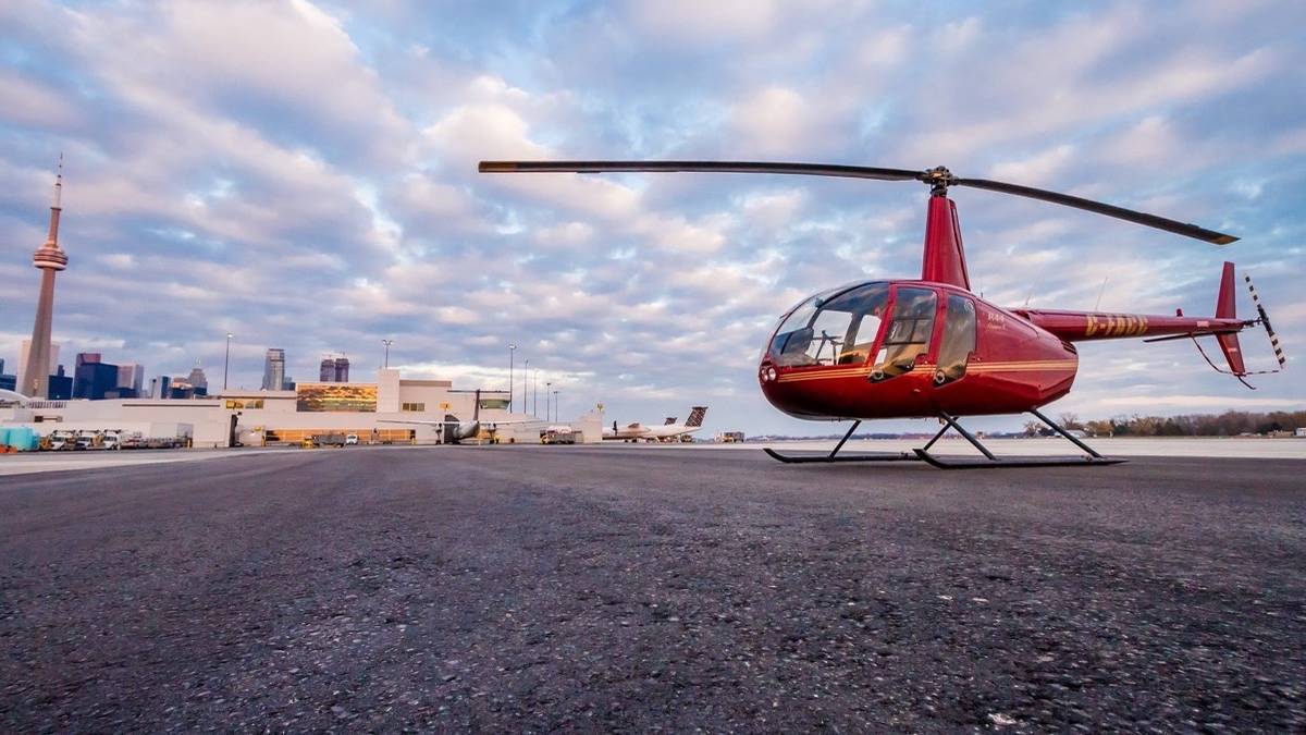 Wide shot of red helicopter sitting on airstrip with CN tower and Toronto skyline in background