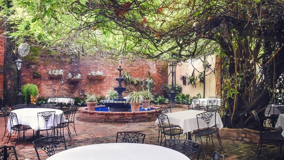 Outdoor brick courtyard with a fountain and chairs with white table cloths and greenery