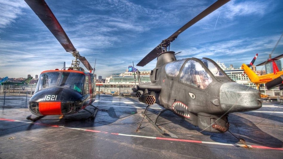 Two war helicopters sitting on a concrete deck