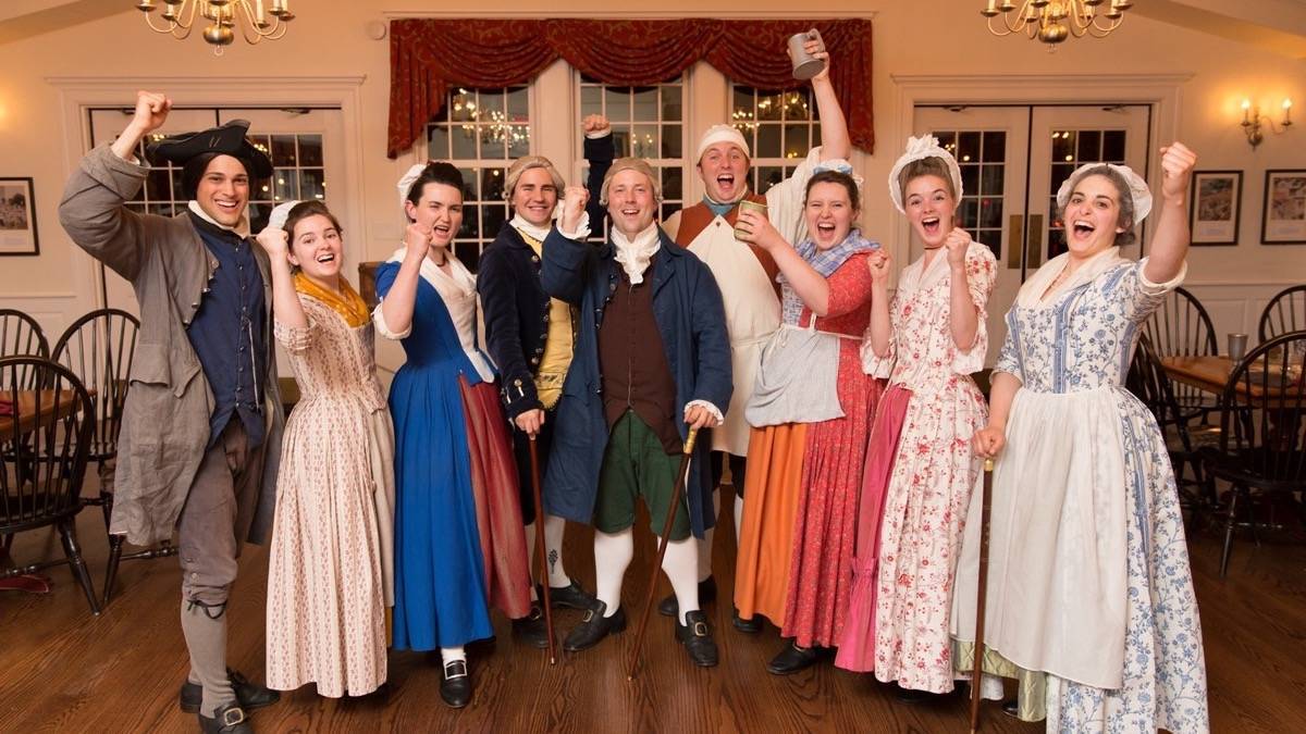 A group of people dressed in Colonial attire celebrating in a room at the Boston Tea Party Ships & Museum