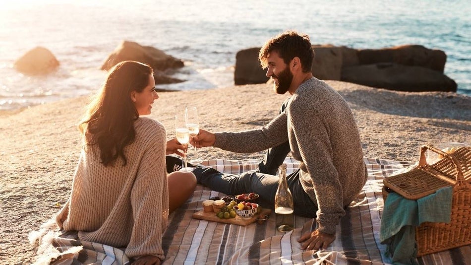 Couple sitting on a blanket with a wine and cheese board next to the ocean on the beach