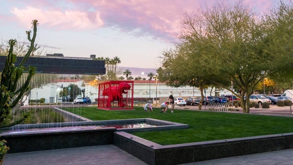 green lawn with red dinosaur sculpture in a red cage at dusk