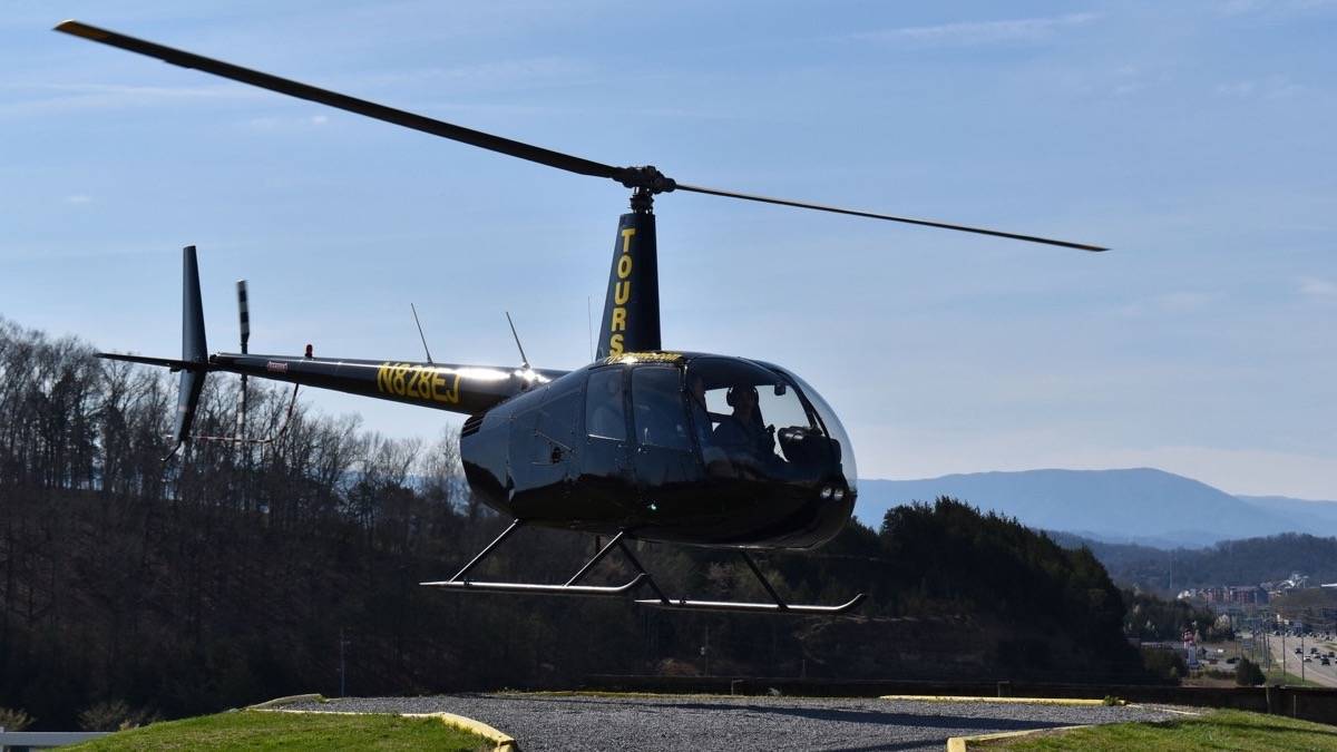 Dark helicopter hovering just above the ground with the smoky mountains in the background