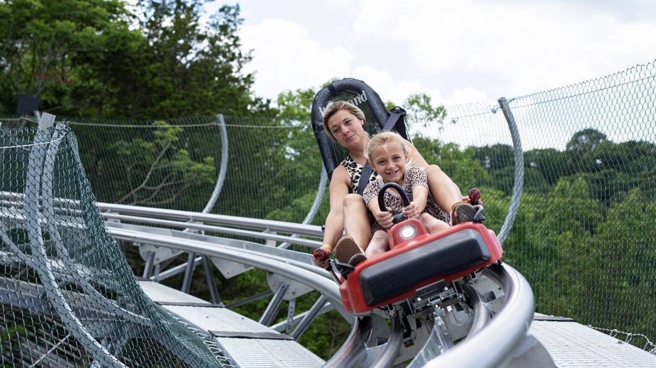 Mom and daughter on a mountain rail coaster with green trees surrounding them