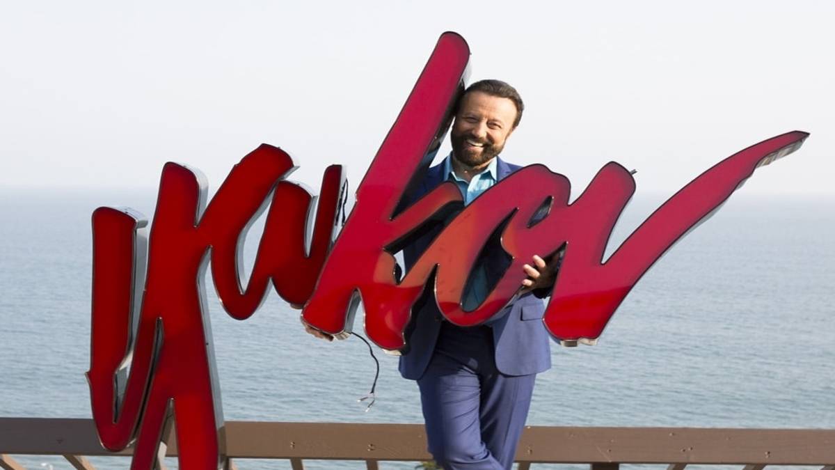 Man holding a red "Yakov" sign in front of the ocean