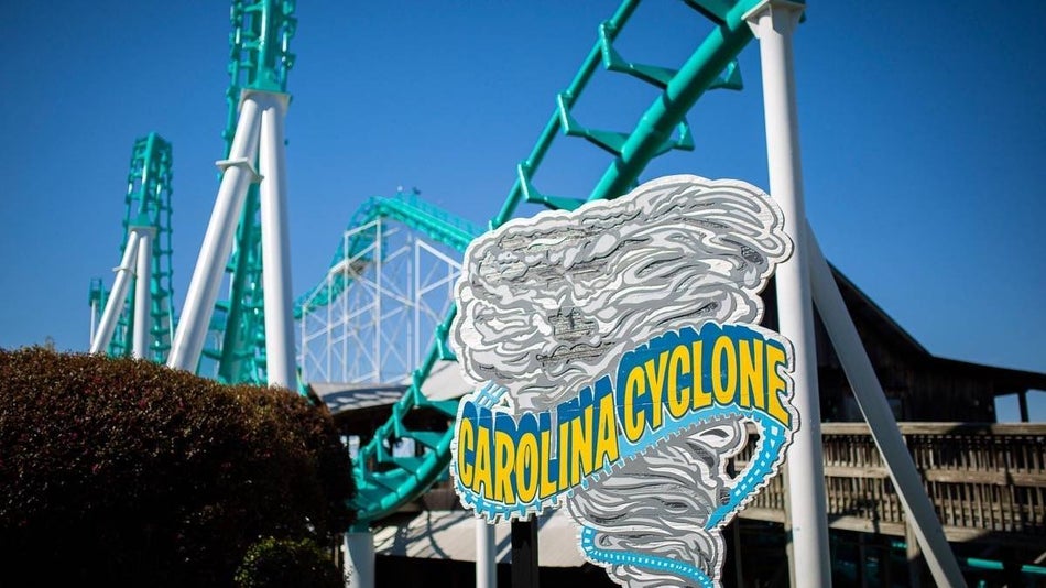 Front sign of the Carolina Cyclone ride with roller coster in background under a blue sky