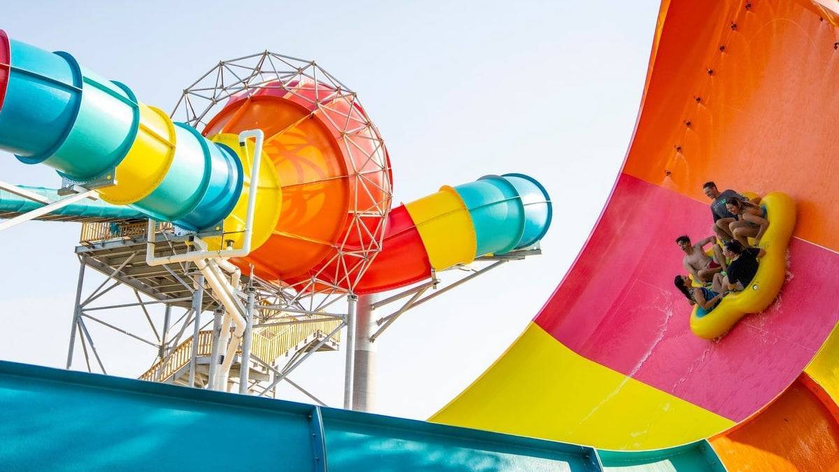 Multicolored waterslide twisting through the sky with a group of people siding down on a yellow tube