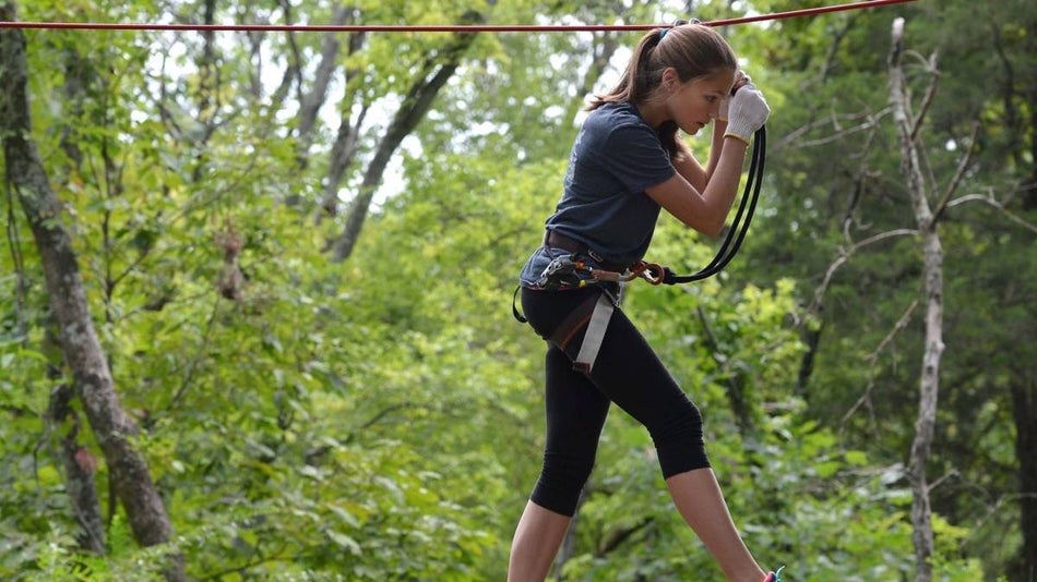 Girl holding onto a zipline while walking on a suspended bridge