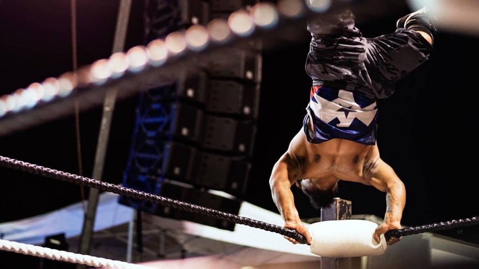 Micro wrestler doing a handstand on the rope surrounding a wrestling ring