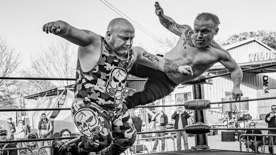 Black and white photo of two men wrestling in an outdoor arena surrounded by a crowd