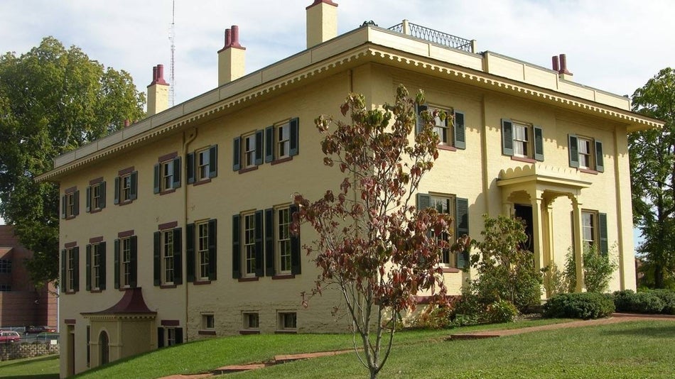 Historic yellow house with many windows and chimneys and green lawn surrounding