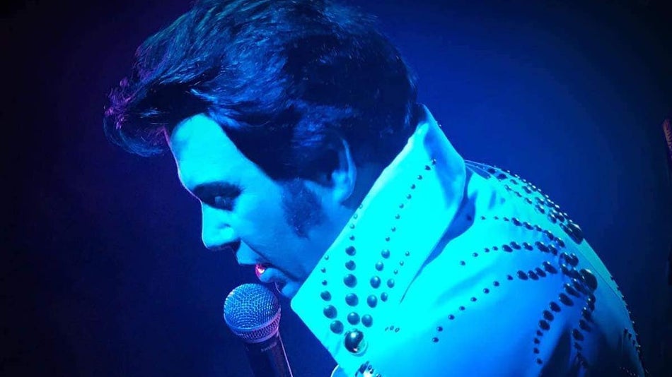 Close up of Elvis performer in a white jacked with a blue light shining on him