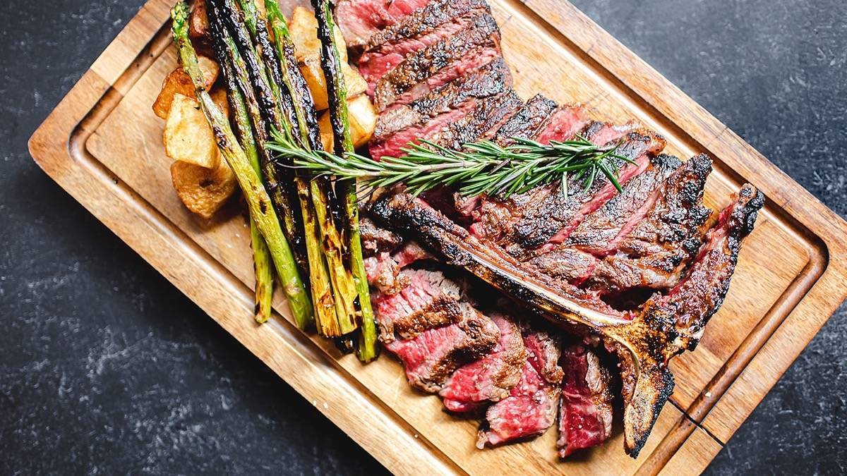 Steak on a cutting board with roasted asparagus and potatoes surrounding it