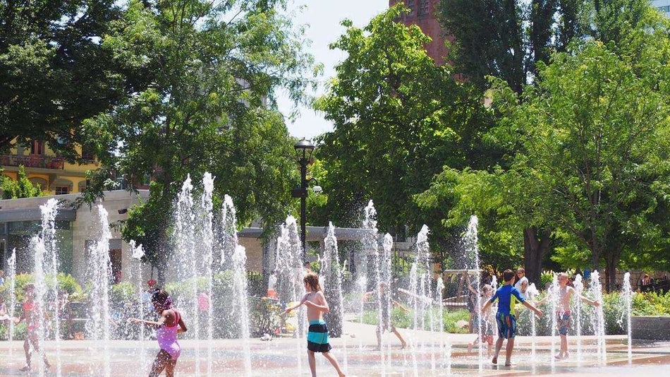 Children playing in many fountains with green trees in the background