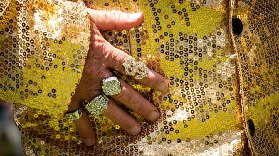 Closeup of a gold glitter jacket with a hand pressed to it wearing gold bling rings