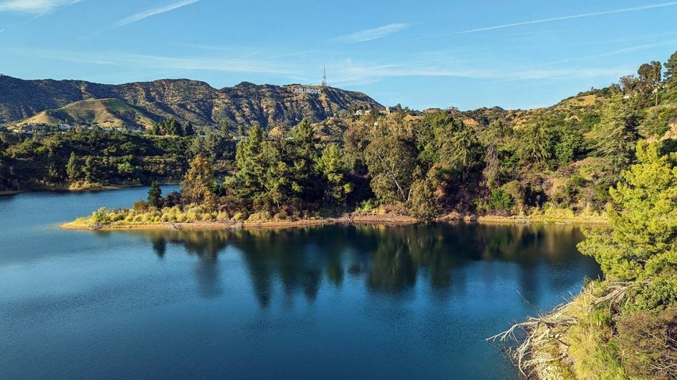 View of Hollywood Reservoir with Hollywood Sign in the background under a blue sky surrounded by green trees