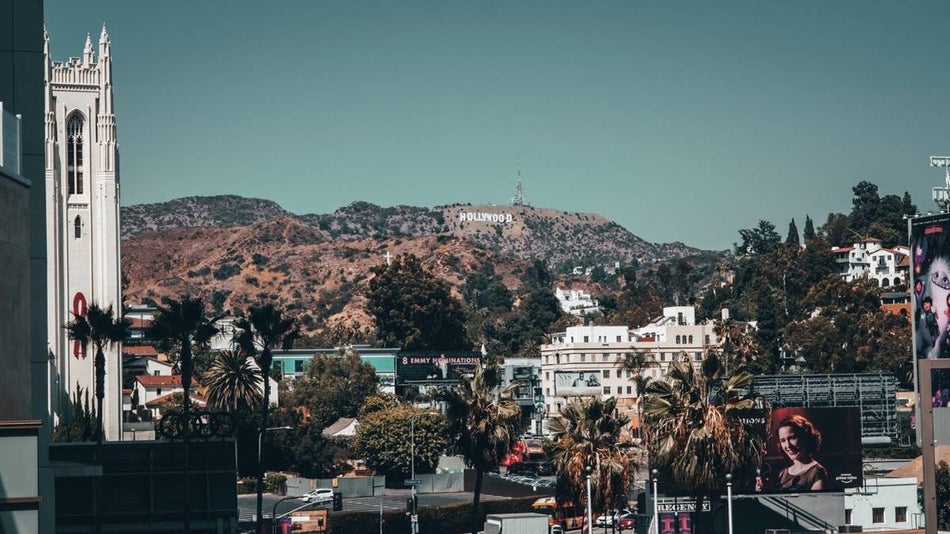 View of hollywood sign with a white church in the foreground as well as city streets and palm trees