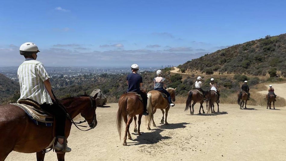 People riding on horseback on a dirt road with los angeles in the background