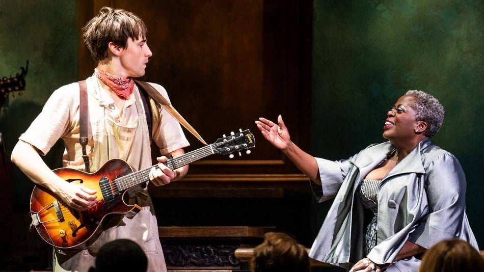 Man holding guitar next to a woman kneeling on stage