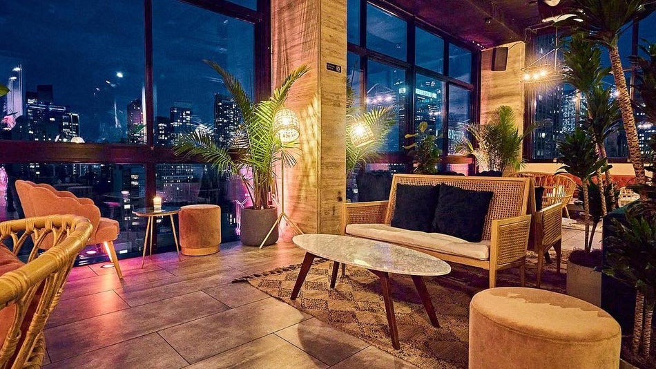 Bar seating area with velvet chairs, wicker furniture and tropical plants overlooking manhattan