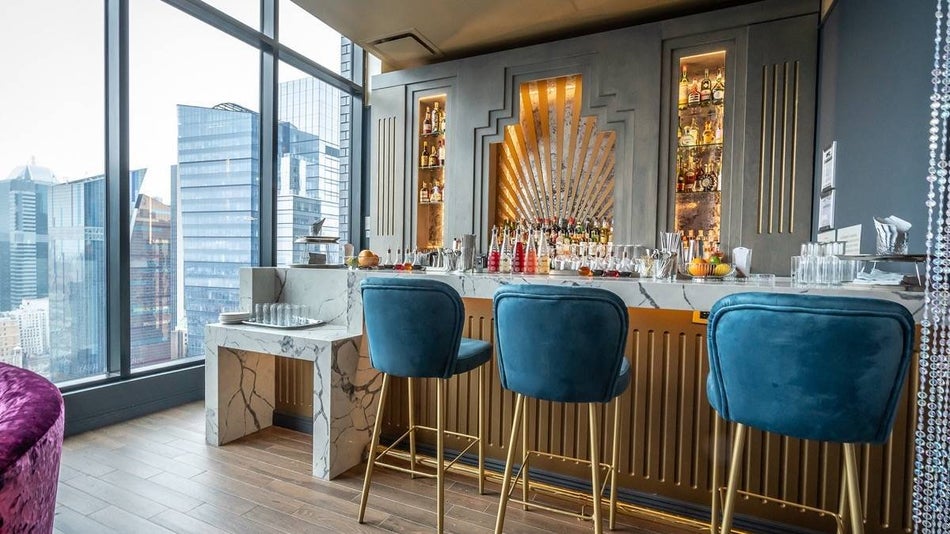Blue velvet barstools at a marble bar with a view out over manhattan