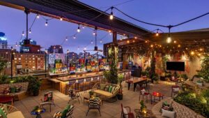Dimly lit rooftop bar with colorful furniture and string lights overlooking manhattan