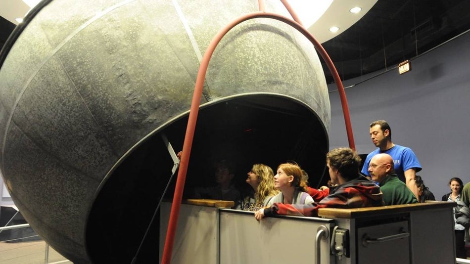 People in a metal seating box looking at a large metal dome