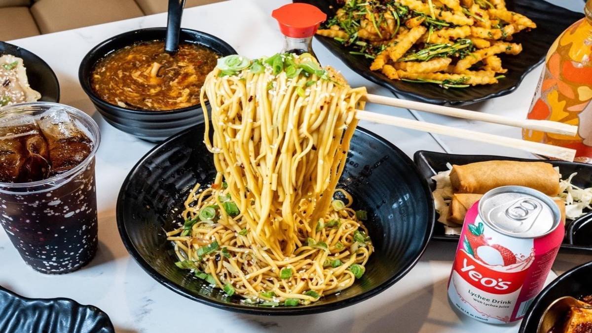 Asian foods, including ramen, soup and spicy fries are on a table with couple of sodas