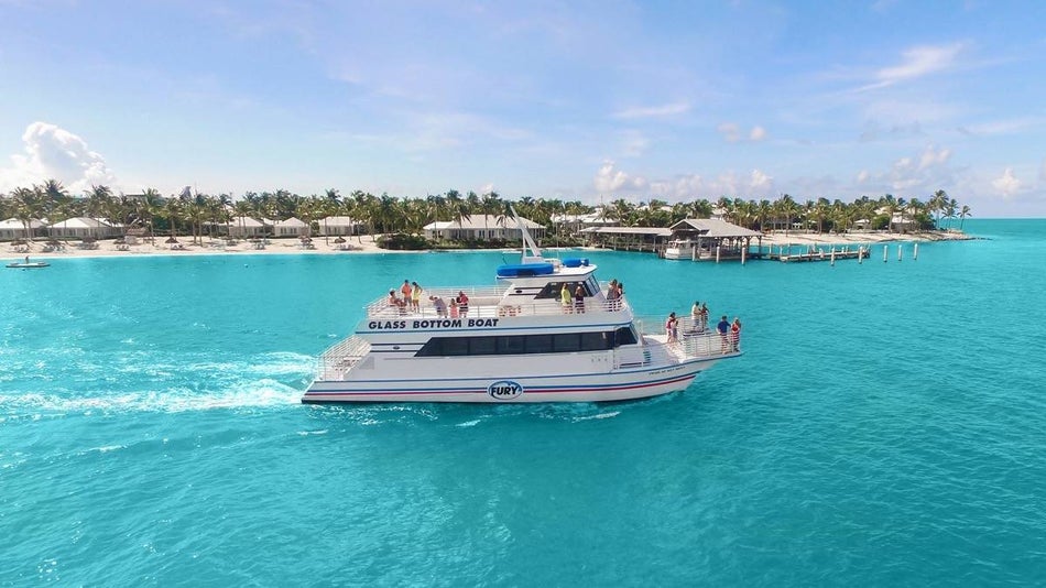Wide shot of a white catamaran with people sailing with glass bottom boat key west under a blue sky with palm trees on the shore in the background
