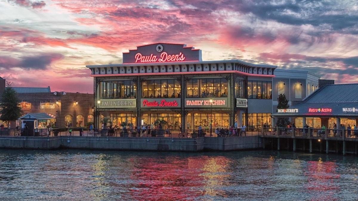 Exterior view of Paula Deen's Family Kitchen building on a waterfront at sunset