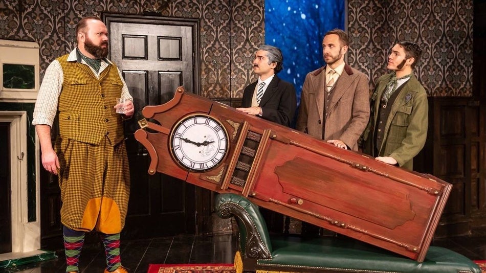 Three cast members holding a grandfather clock while looking at a fourth cast member standing to the side