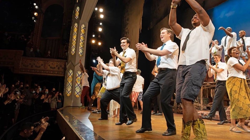 Cast members dressed in white button down tops and black pants on stage