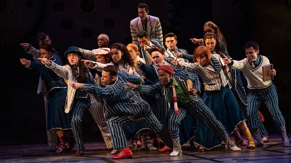 A bunch of cast members in blue striped suits pointing in the same direction off stage
