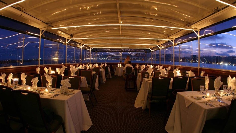 Interior of a dinner cruise with table covered with white clothes and dinnerware at dusk