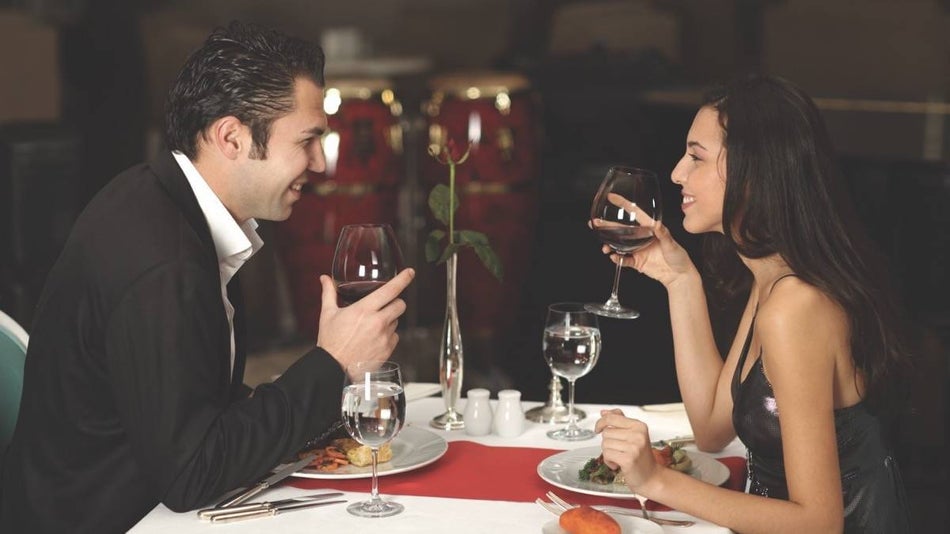 A couple in formal clothing holding wine glasses looking at each other while at a dinner table