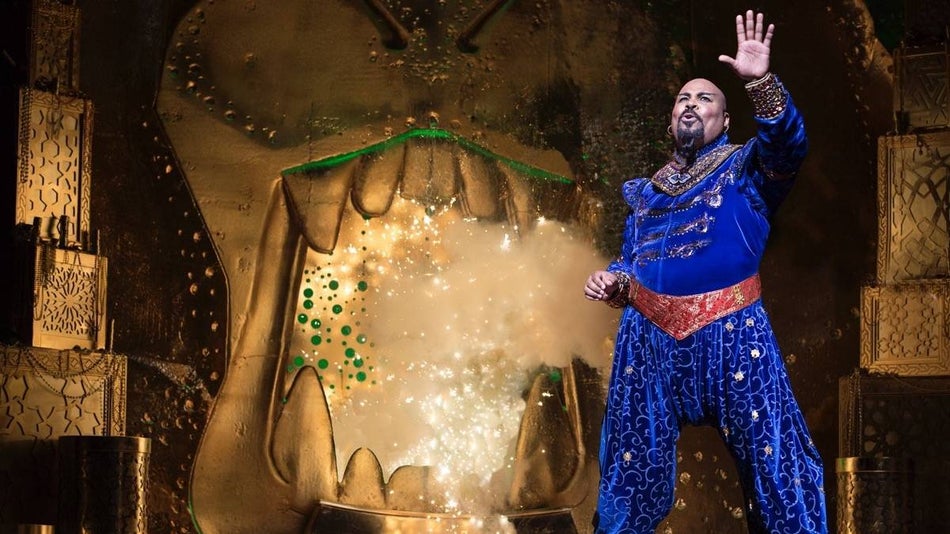 Cast member dressed in a blue velvet pant suit on stage performing in the Aladdin show