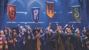 Cast playing children at Hogwarts cheering with their house flags raised