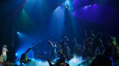 Cast members looking up at a witch hovering in the air
