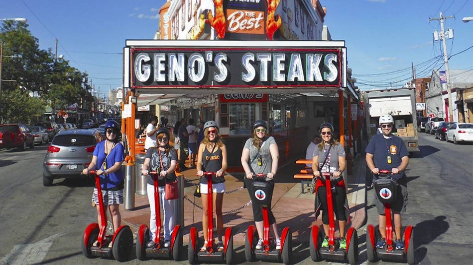 Several people on red segways in front of a cheesesteak restaurant in philly