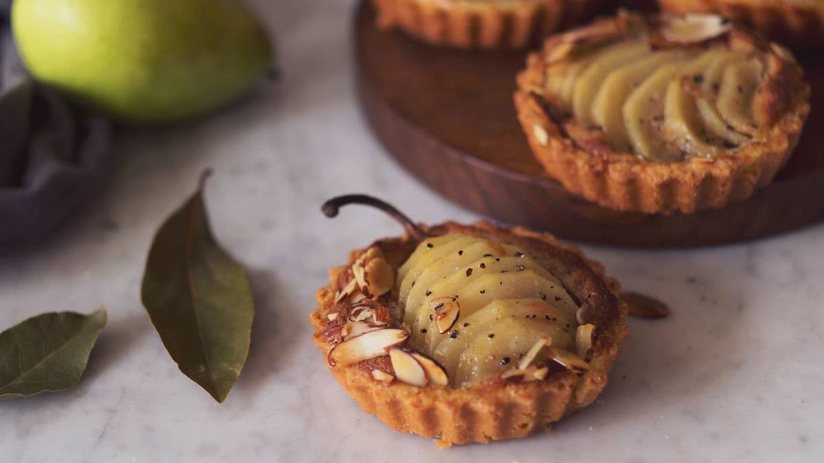 Pear tartlets with a leaf and pear styled around it on a white background