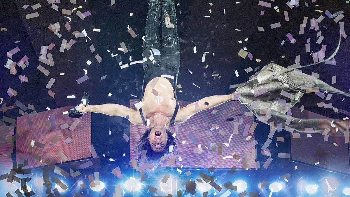 Man hanging upside down with a coat in his hand and confetti falling all around him