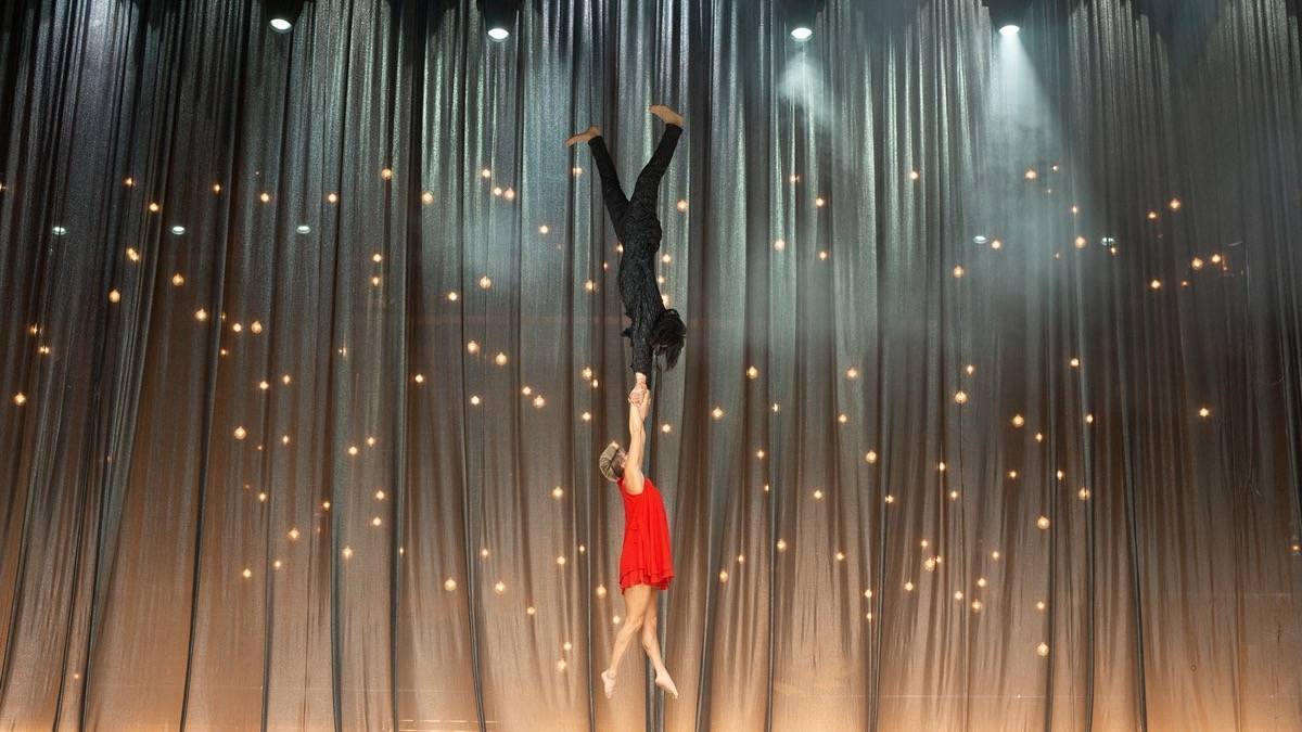 Man suspended in the air holding onto the hands of a woman in a red dress