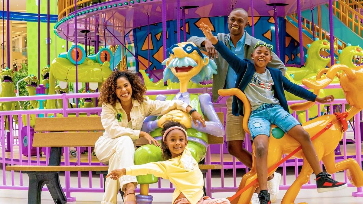 Family sitting on a bench with a cartoon character statue in front of a colorful carousel