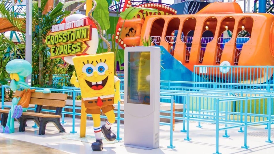 Spongebob character with a thumbs up next to a bench with squidward character in front of an orange submarine ride