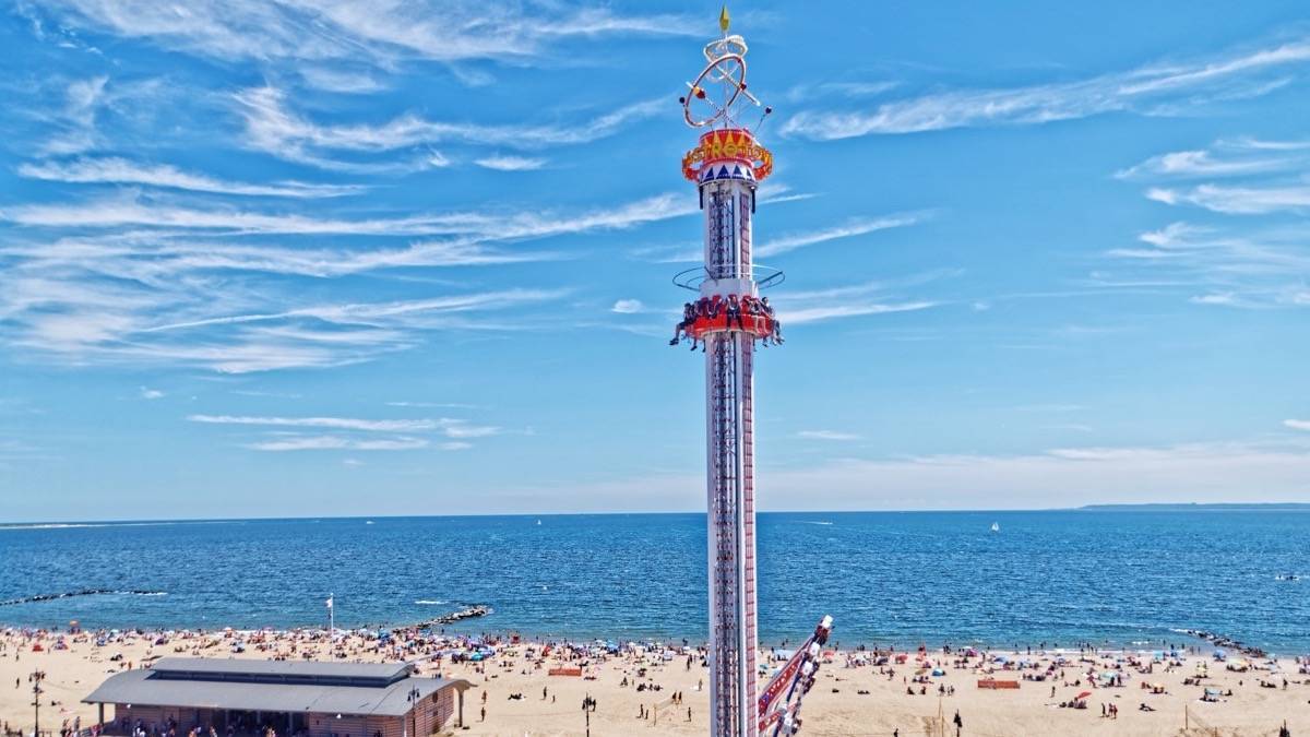 A tall drop tower amusement park ride with the ocean in the background