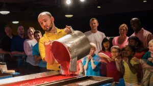 man holding a big pot full of red wax pouring it into molds in front of a small crowd of people at the Crayola Experience in Orlando