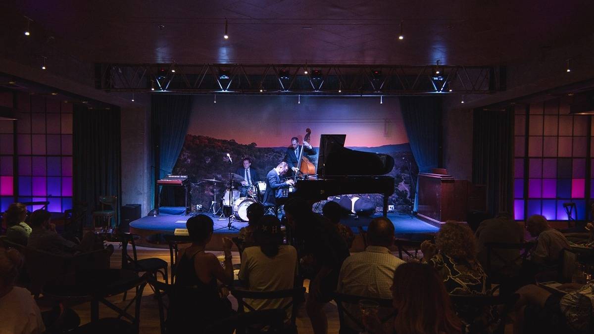 Shot of stage with musicians playing a piano, drums, and a base in a jazz club